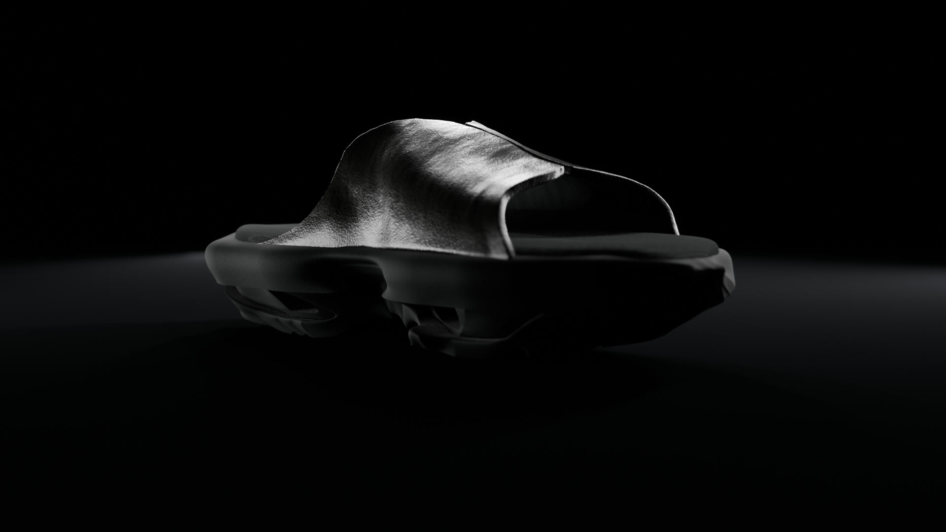 A black 3D-printed TPU geta slide with a leather upper, lit from behind on a black studio floor